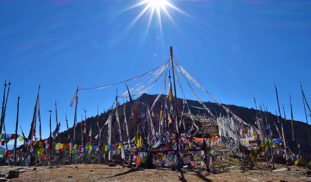 A panoramic vista from Chele La Pass, showcasing the snow-capped peaks of the Himalayas and the winding mountain road below.